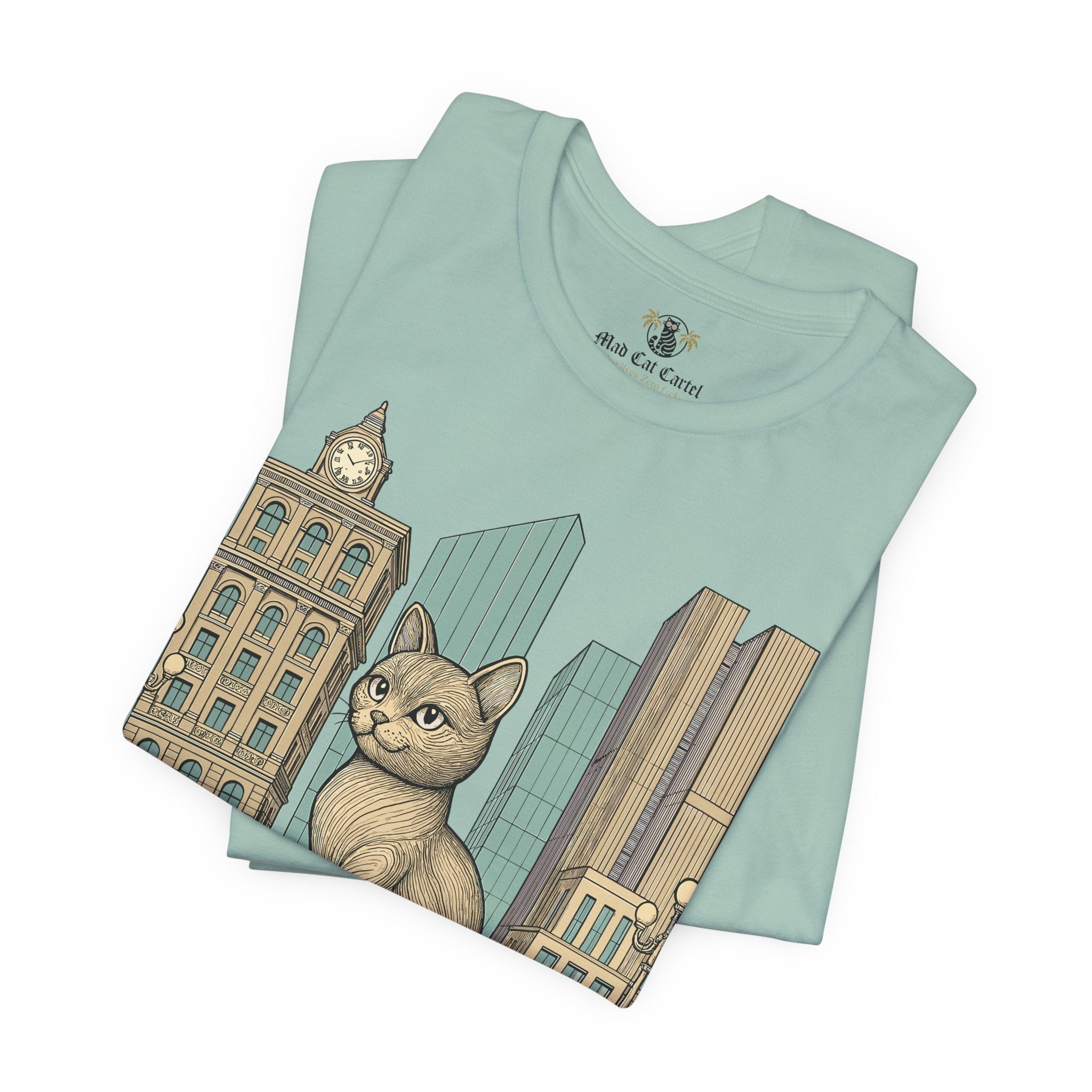 Funny adult shirts – dusty blue unisex tee folded, Meowschino city cat statue print visible