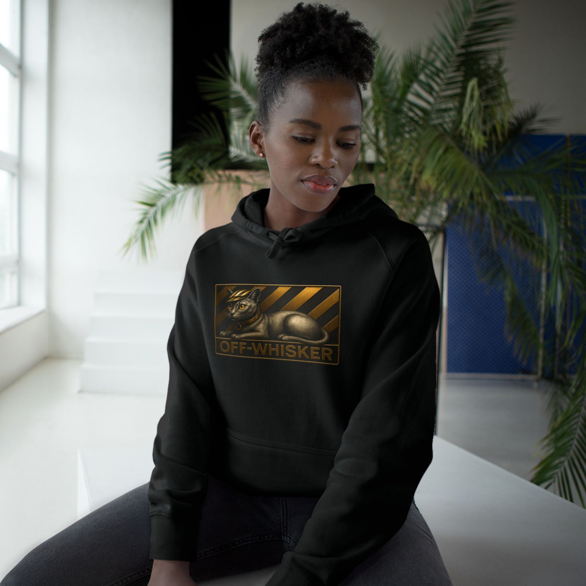 Woman seated in Off-Whisker bronze cat emblem black hoodie, stylish cat hoodie for woman