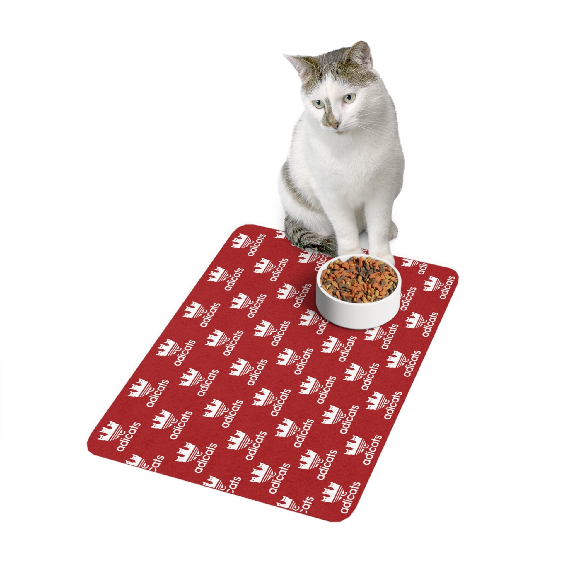 Cat sitting on a red cat feeding mat with Adidas logo next to a white bowl of cat food