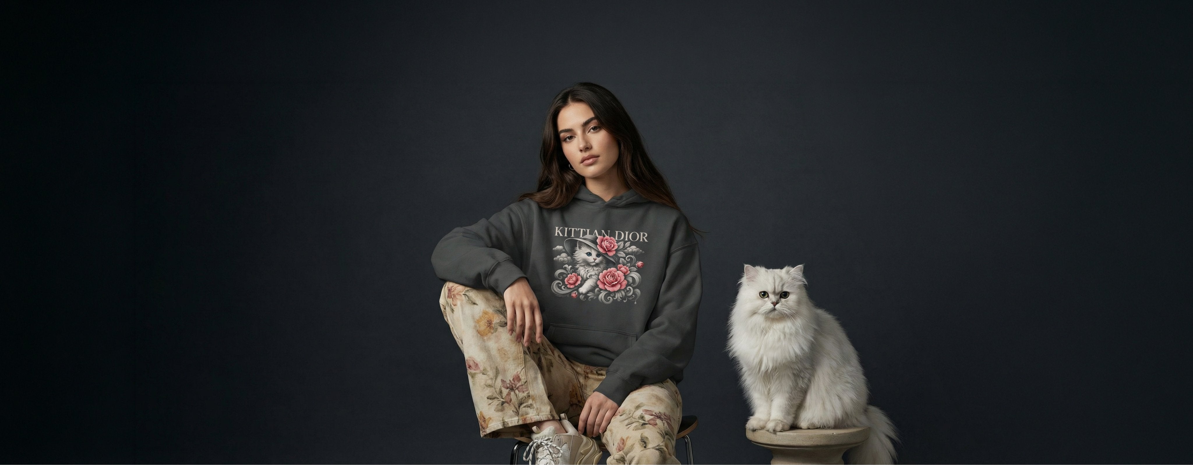 woman wearing a dark grey funny cat hoodie for women with Kittian Dior parody graphic next to a white cat, desktop banner image