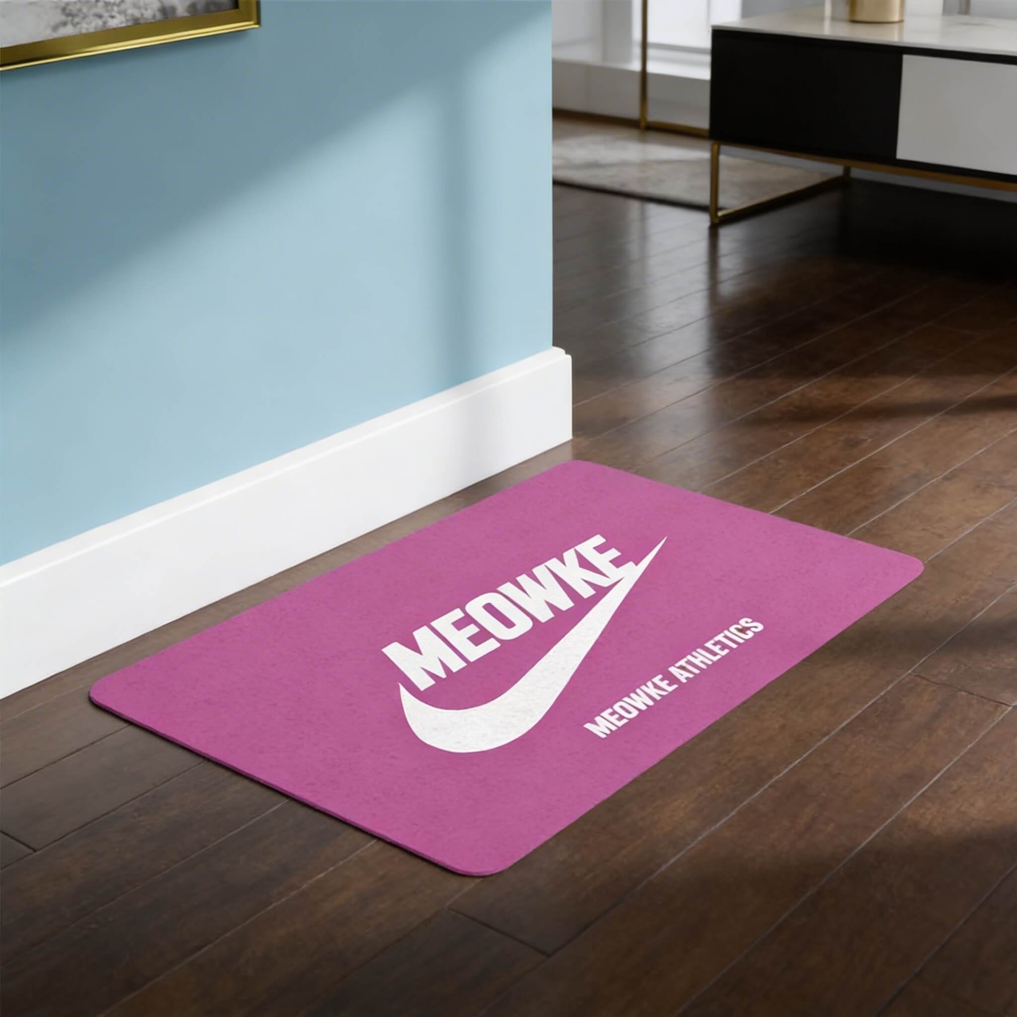 Pink Meowke cat food mat with sporty logo print on dark wood floor