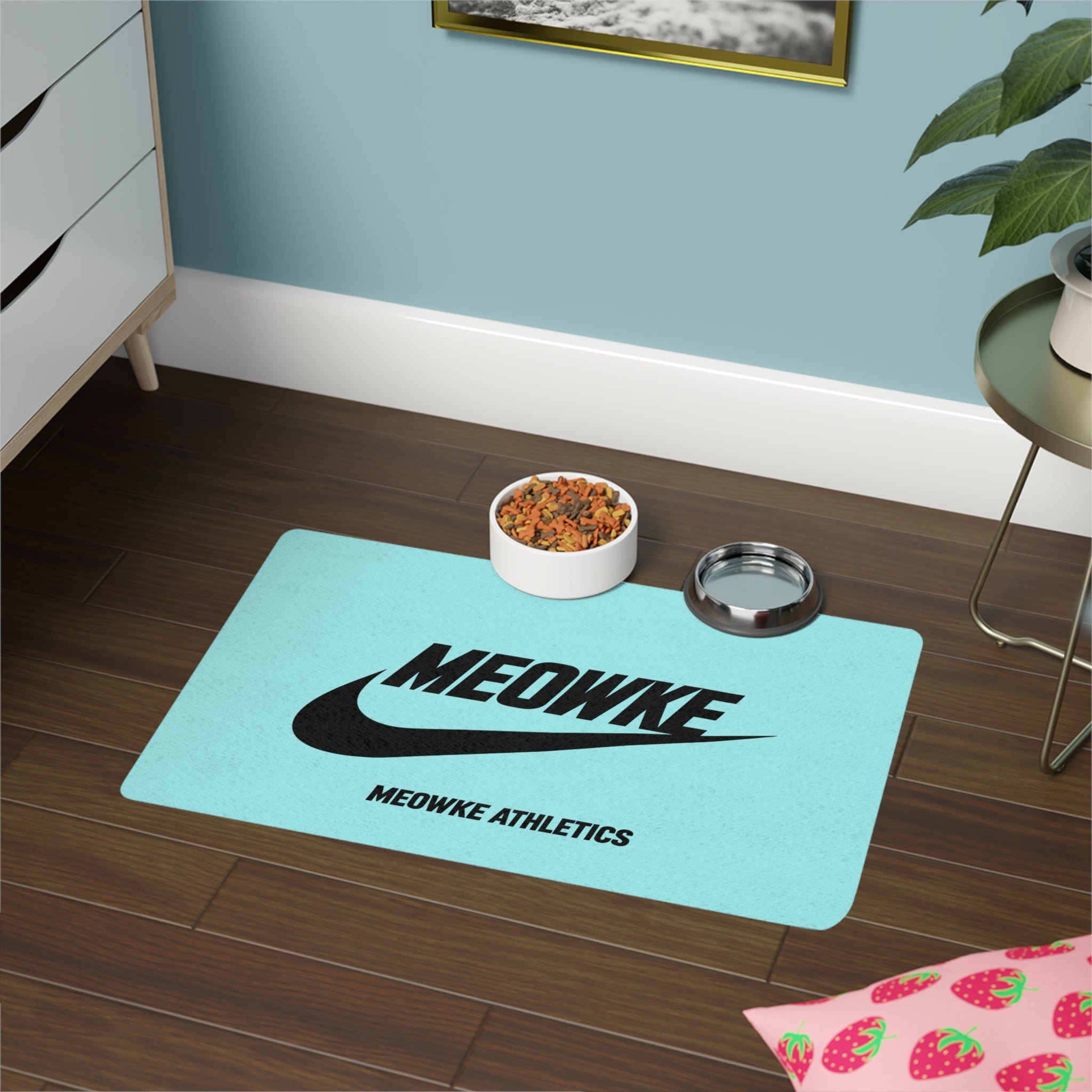 Meowke teal cat food mat with food and water bowls on a clean athletic logo layout
