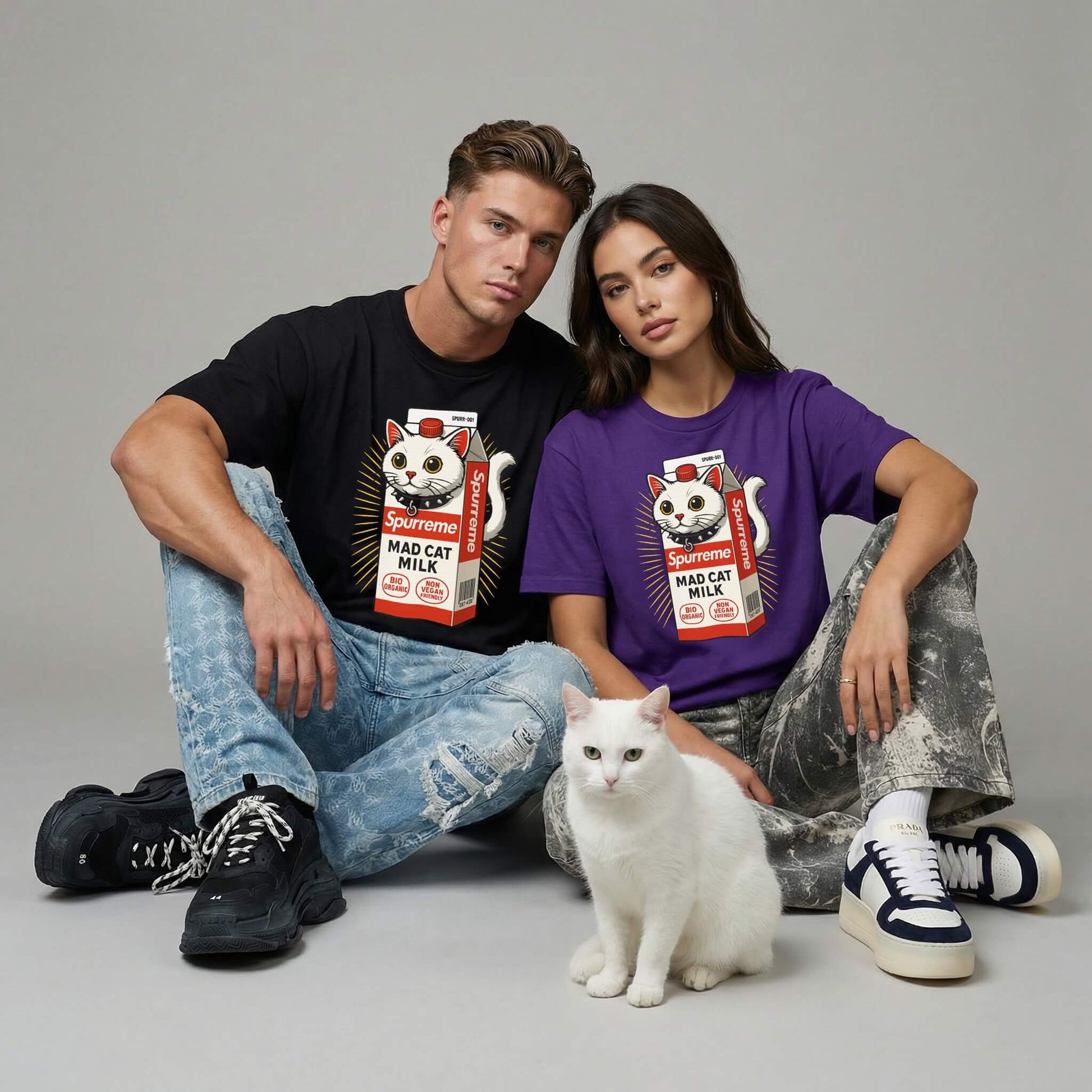 man and woman wearing Spurreme cat matching t-shirts with a cat graphic and a white cat sitting between them on a gray background.