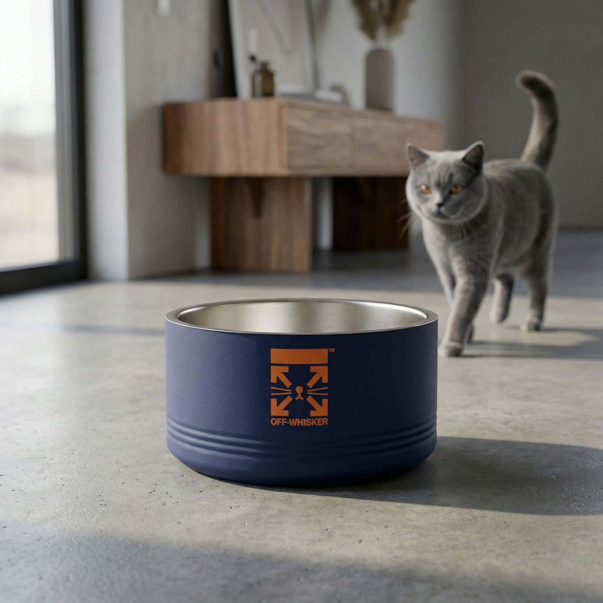 Blue pet bowl with a logo on a concrete floor, with a cat in the background