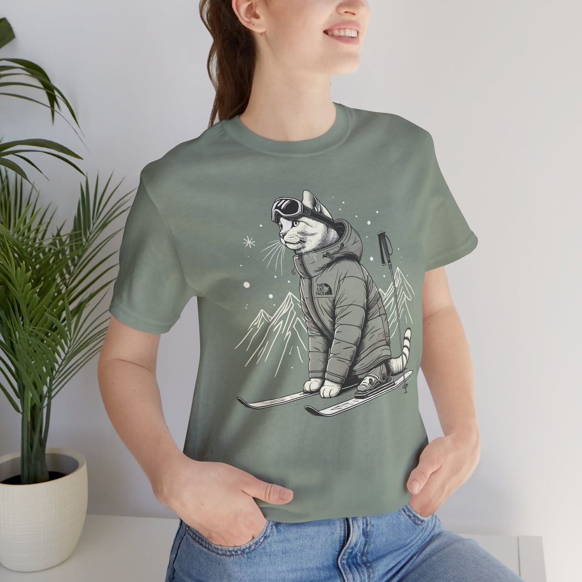 The Cat Face Alpine Explorer Graphic T-Shirt in sage, worn by a female model