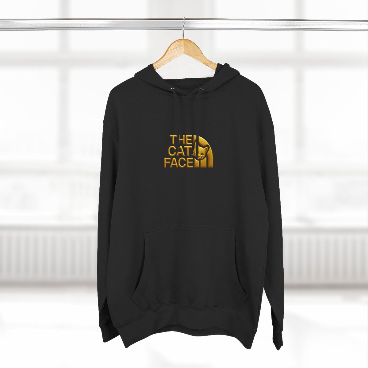 The Cat Face Gold Chest Logo & Back Puffer Cat Graphic Hoodie in black, on a hanger