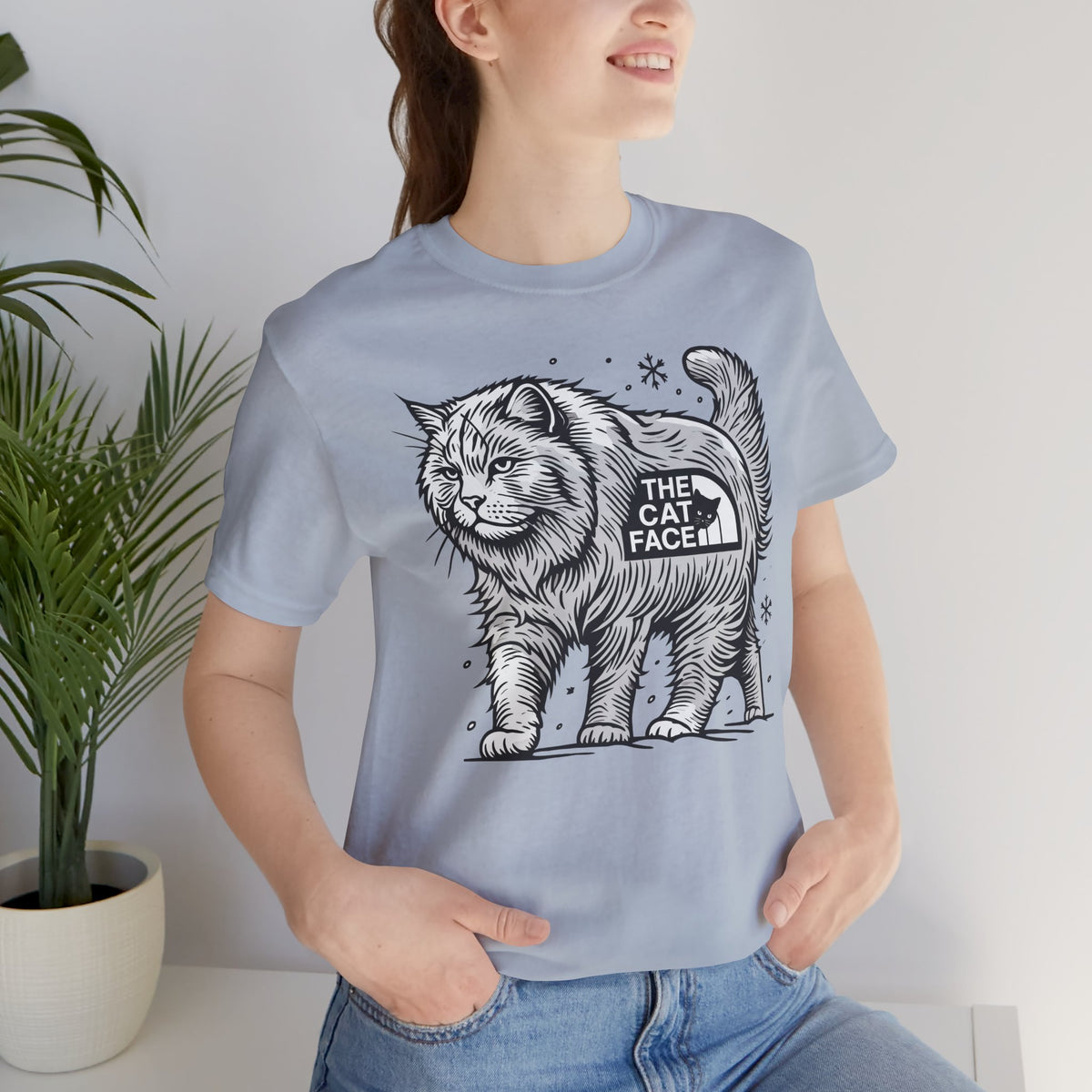 The Cat Face Snow Explorer Cat Graphic T-Shirt in light blue, worn by a female model