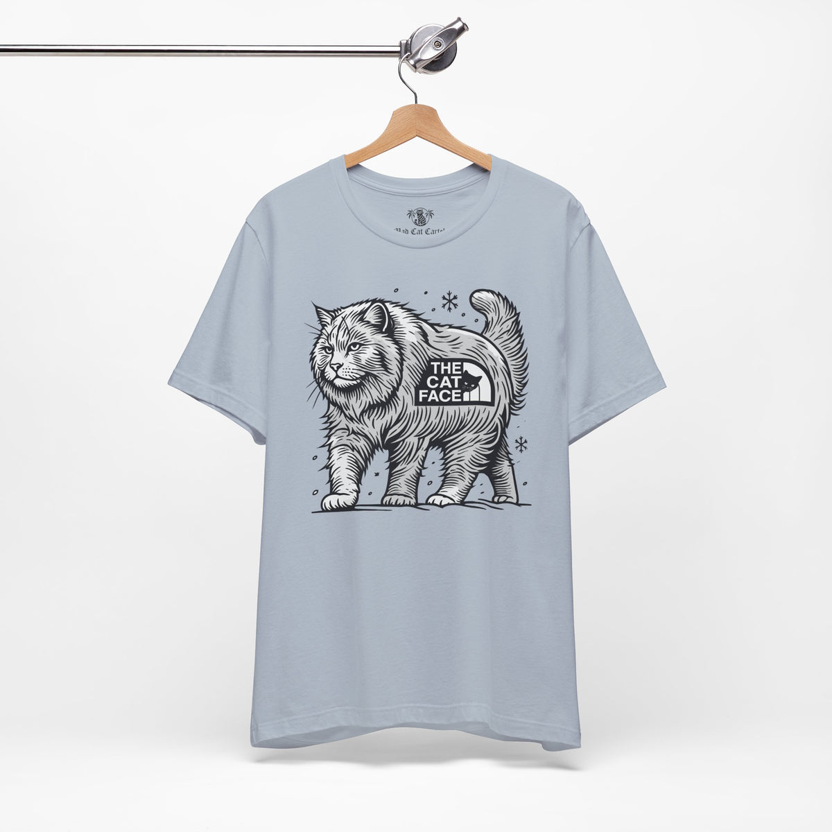 The Cat Face Snow Explorer Cat Graphic T-Shirt in light blue, on a hanger