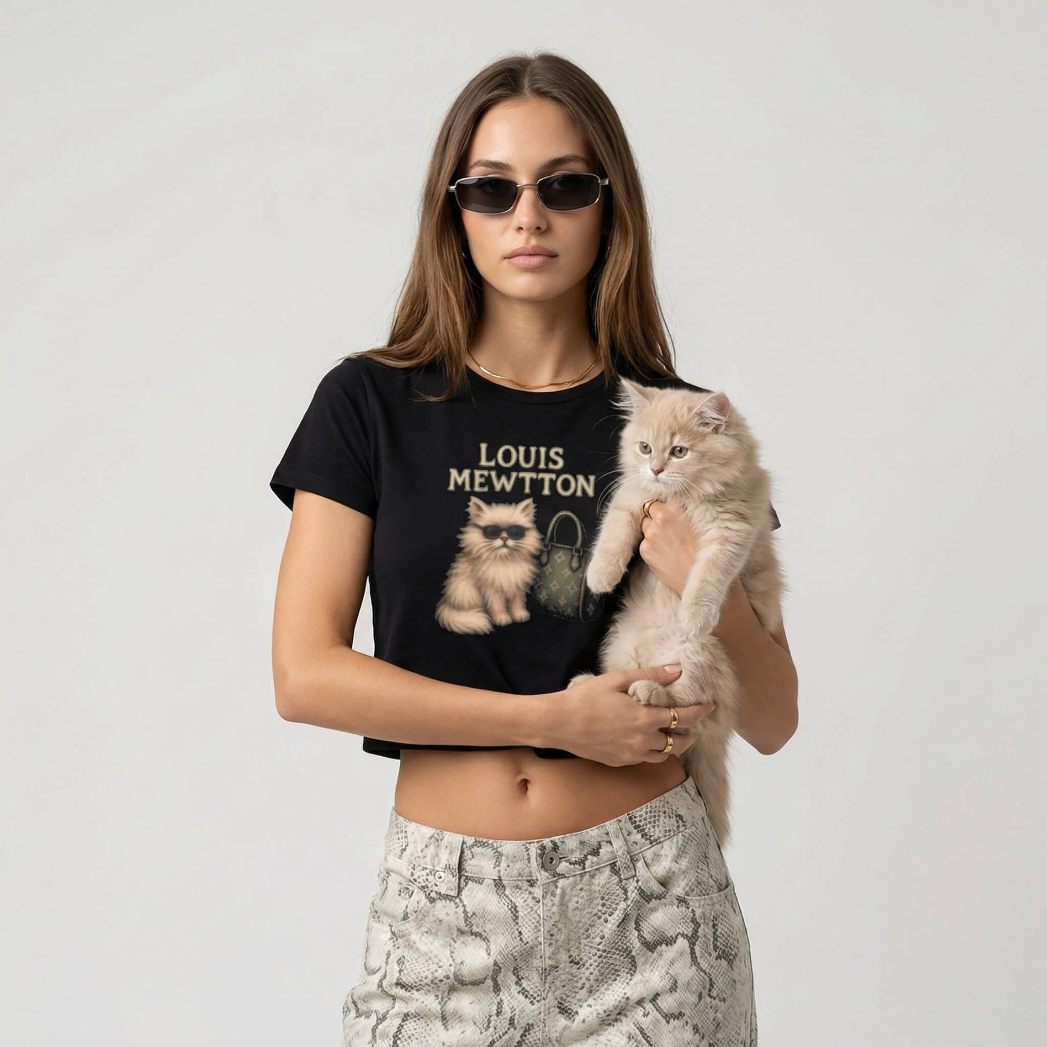 Woman wearing a black designer t-shirt with cat graphics and text, holding a cat, on a plain background